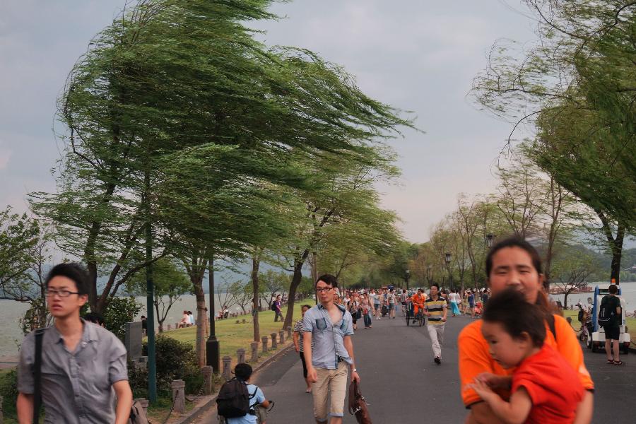 People walk in strong wind beside the West Lake in Hangzhou, capital of east China's Zhejiang Province, July 30, 2013. Hangzhou City underwent a rainmaking on Tuesday afternoon. (Xinhua/Li Zhong)