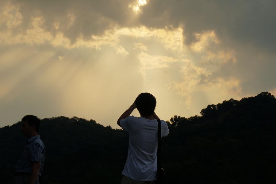 A visitor takes photos of the sunshine through clouds in the sky above the West Lake in Hangzhou, capital of east China's Zhejiang Province, July 30, 2013. Hangzhou City underwent a rainmaking on Tuesday afternoon. (Xinhua/Li Zhong)