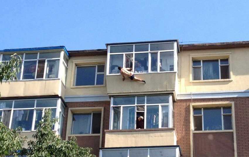 A man tries to jump from the building to commit suicide in a residential area in Changchun, captial of China's Jilin Province, July 31, 2013. While he jumped out of the window, his leg was caught by his wife. Later he was rescued by the neighbors and policemen. (Photo/Xinhua)