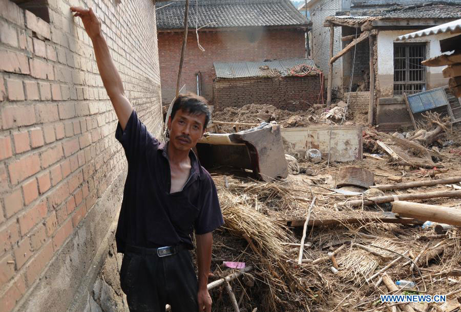 A villager surnamed Zhang of the Liulin Village, introduces the height of the flood in his courtyard in Niangniangba Town, Qinzhou District of Tianshui City, northwest China's Gansu Province, July 31, 2013. More than 20 people were dead or missing and about 1.22 million people were affected by the landslides and floods caused by strong rainfall in Tianshui in recent days. (Xinhua/Bai Liping)