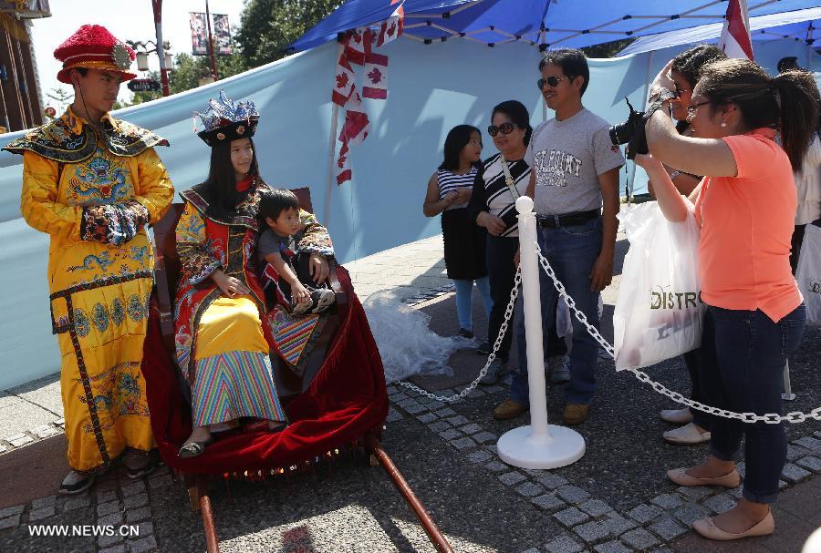 A visitor poses with performers in Chinese costumes at the Chinatown festival held in Vancouver, Canada, Aug. 10, 2013. The 14th annual Chinatown festival showcased the attractiveness of Chinese culture and brought about 60,000 visitors to experience the biggest multicultural summer celebration. (Xinhua/Liang Sen)