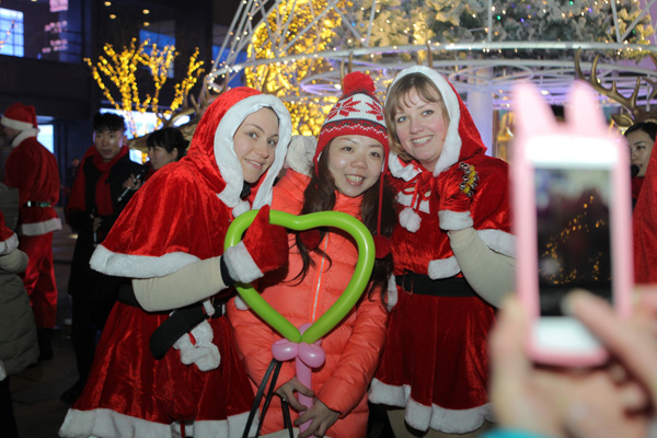 A Beijing resident poses with foreign performers in the city's Sanlitun shopping district to celebrate Christmas Eve on Tuesday. (China Daily/Wang Jing)