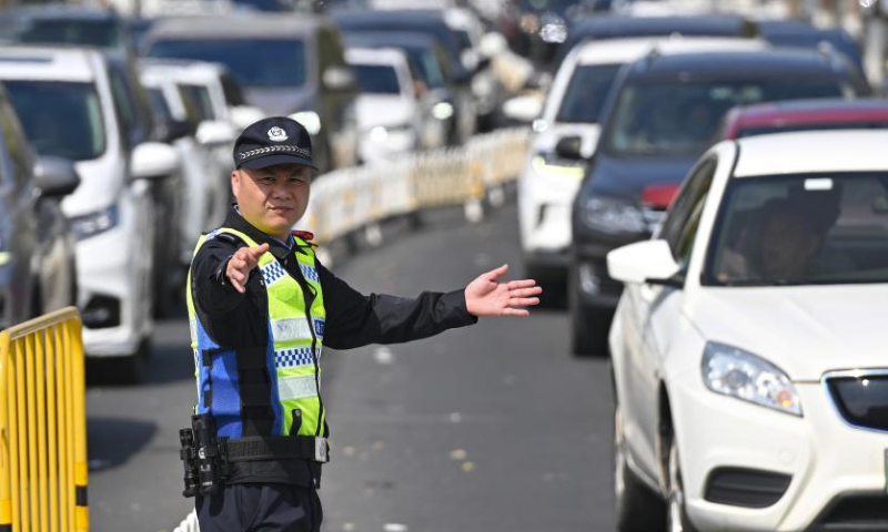 A police officer direct traffic near a port in Haikou, south China's Hainan Province, Feb. 17, 2024. Qiongzhou Strait witnessed a peak of travel rush of returning passengers on Feb. 17, the last day of the Spring Festival holiday.Various actions were taken by local authorities to ensure passengers to cross the strait in an orderly manner including organizing personnel to maintain the queuing order, providing emergency medicines, drinking water and other supplies to drivers and tourists. (Xinhua/Guo Cheng)